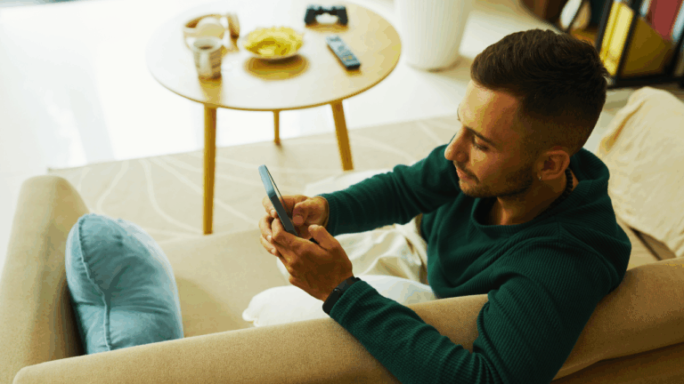 Man sits on couch scrolling on his phone.