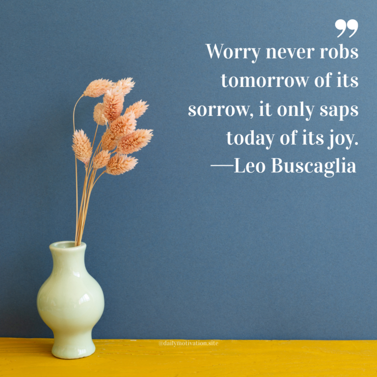 Pale green ceramic vase holding dried wheat stems against a muted blue wall and yellow tabletop.