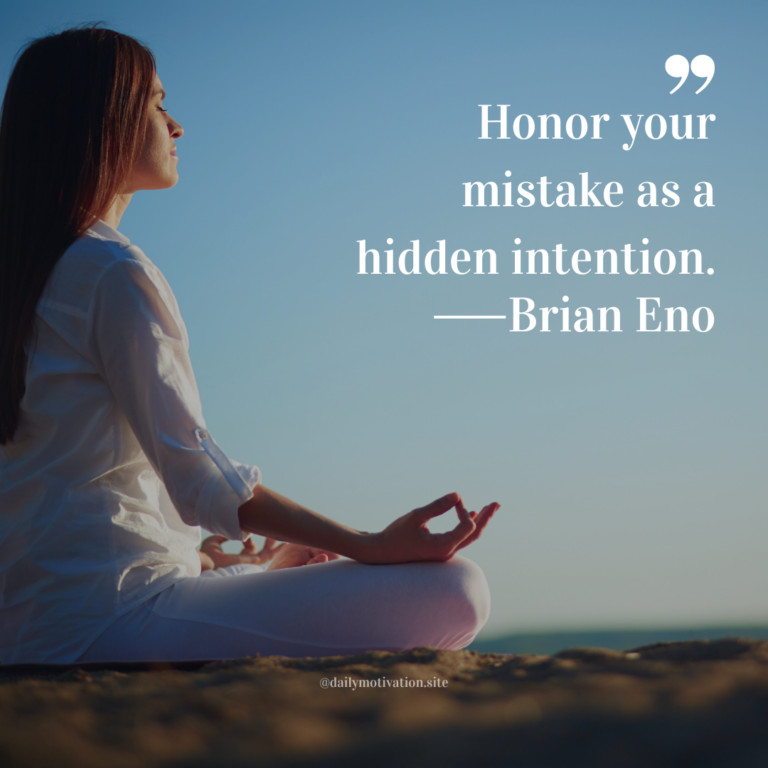 Person seated cross-legged in meditation on a rocky surface under a clear blue sky.