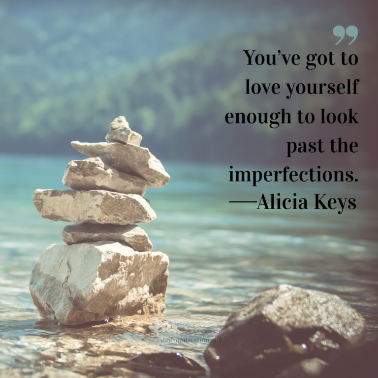 Stack of smooth stones balanced in shallow clear water with mountains blurred in the background.